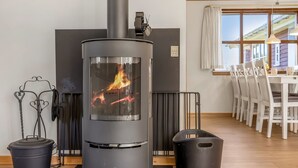 Ein modernes Zimmer mit Kaminofen, Esstisch mit Stühlen und einem fenster mit Vorhängen.