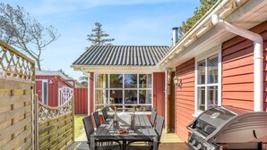 Eine Terrasse mit Tisch, Stühlen und einem Grill, sowie ein rotes Gebäude mit einem Fenster.