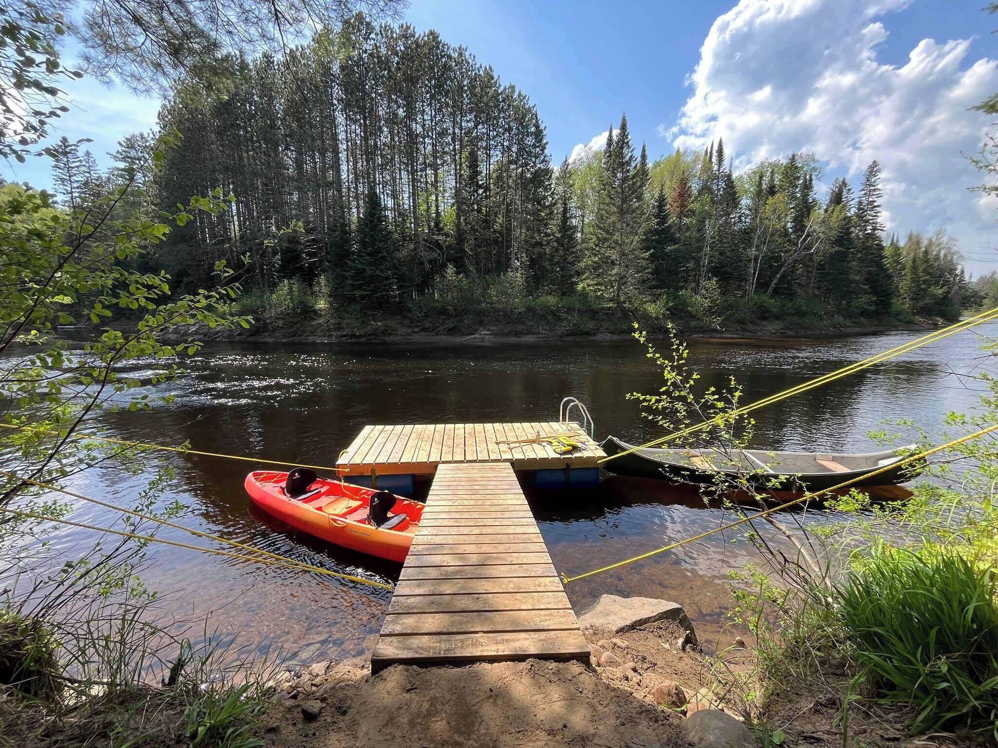 A wooden dock extending into a river surrounded by dense forest.