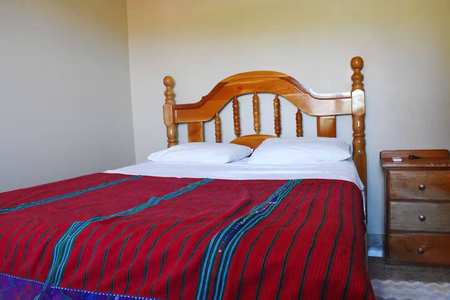 Un lit avec une tête de lit en bois, des oreillers blancs et une couverture à rayures rouges et bleues.