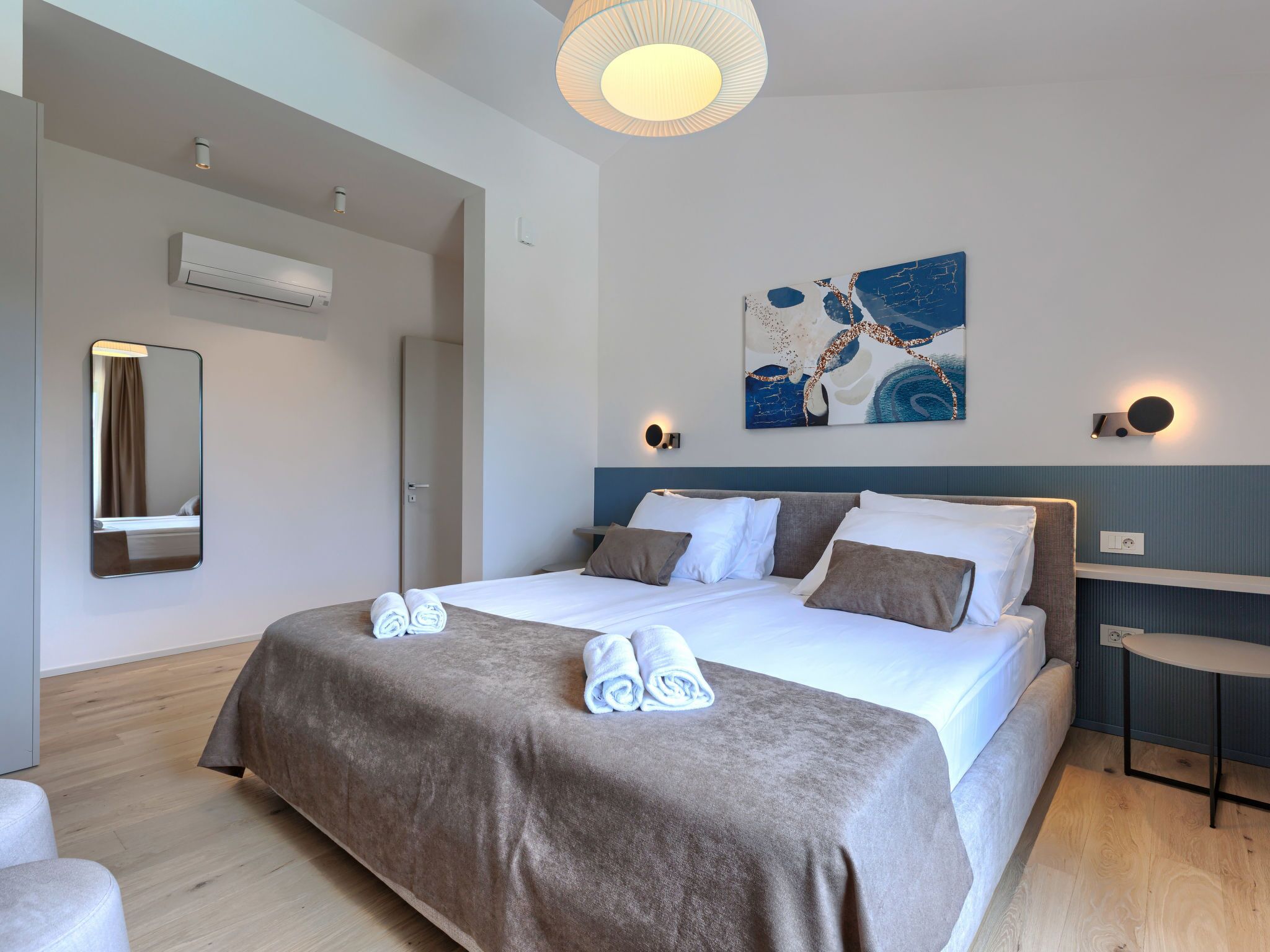 Een moderne hotelkamer met een groot bed, een wandairconditioner, een plafondlamp en een abstract kunstwerk.