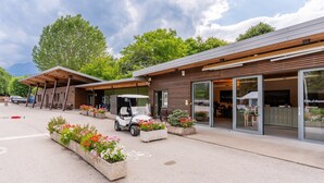Ein modernes Gebäude mit überdachter Außenfläche, einem Golfwagen und Blumenkübeln.