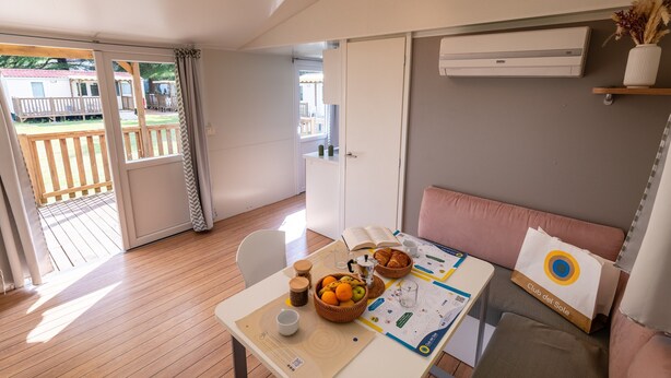 Ein Zimmer mit Holzboden, einem Esstisch mit Obstkorb, einer Couch und einer Klimaanlage.