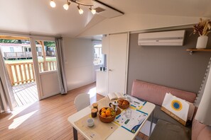 A room with a wooden floor, a dining table with a basket of fruit, a sofa, and an air conditioning unit. - Due Laghi Levico Family Collection (Levico Terme)