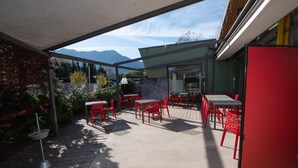 Eine Terrassengruppe mit roten Stühlen und Tischen, einem Betonboden und Blick auf die Berge.