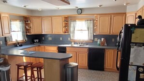 A kitchen with wooden cabinets, a central island with stools, a refrigerator, and a dining area with a table and chairs.