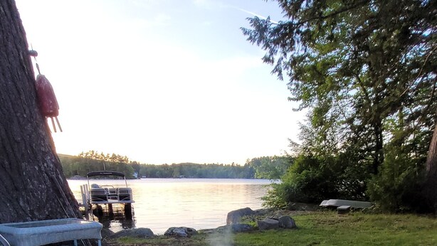 A fire pit made of stones, surrounded by pebbles, with a boat on the water in the background.