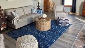 A living room with a sofa, ottoman, and chair, a ceiling fan, and a patterned rug.