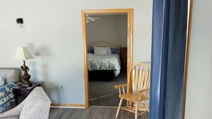 A room with a wooden floor, a sofa, a chair, a wooden table, a mirror, and a blue curtain.