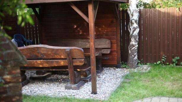 Een houten bankje onder een overkapping, een grindpad en een terras van bakstenen.