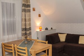 A cozy living room with a brown sofa, a wooden dining table with chairs, and a small side table with a lamp. - Holiday Apartment for 4 People, Rowy (Ustka)