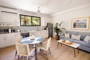 Una cocina moderna con armarios blancos, un refrigerador de acero inoxidable y un comedor con sillas de mimbre y una mesa redonda.