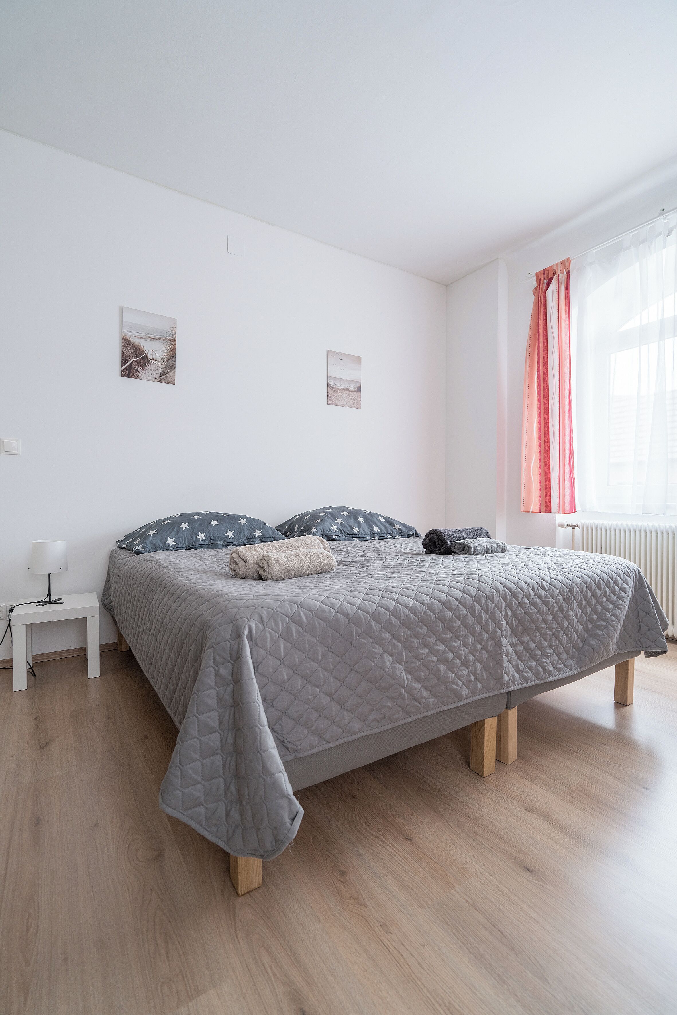 Un dormitorio ordenado con cama, mesita de noche y ventana con cortinas.