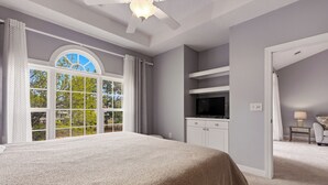 Ein Schlafzimmer mit einem großen Bett, einem Deckenventilator, einem Fernseher und Blick durch ein Fenster.