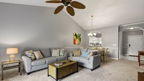 Ein Wohnzimmer mit zwei Sofas, einem Couchtisch, einer Lampe, einem Deckenventilator und einem Essbereich mit Stühlen und einem Tisch.