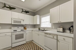 Una cocina con gabinetes blancos, un microondas, una estufa, un lavamanos y un tostador.