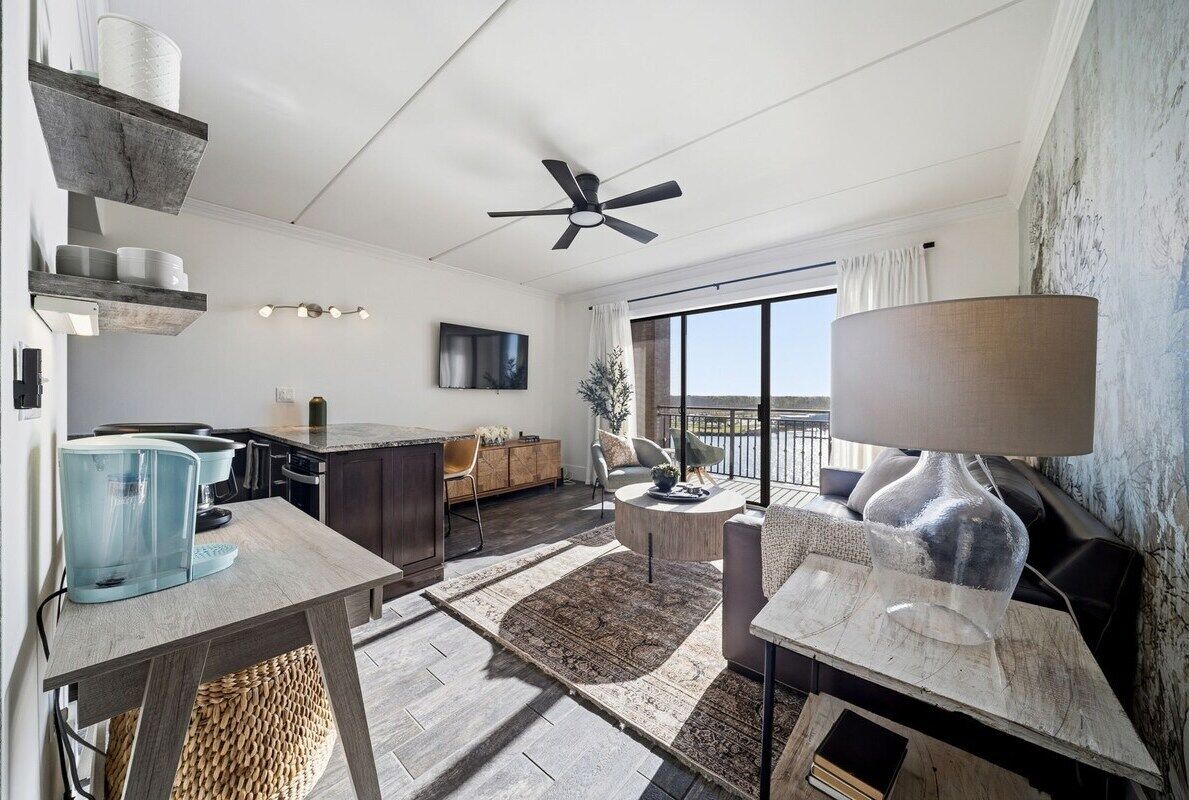 A modern living room with a dining area, a ceiling fan, a large window, and a view of the outdoors.