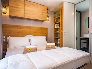 Ett hotellrum med en sänggavel i trä, en stor säng med vita sängkläder, en garderob i trä och ett litet badrum som syns genom en öppen dörr.