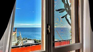 Ein Fenster mit Blick auf den Ozean und einem roten Zaun davor.