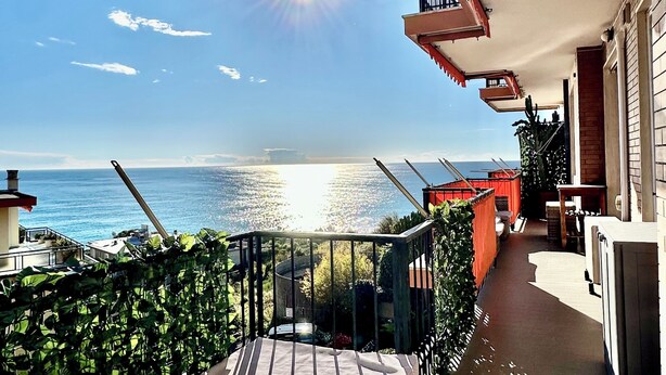 Ein Balkon mit Meerblick, eine Rattan-Couch und ein kleiner Tisch.