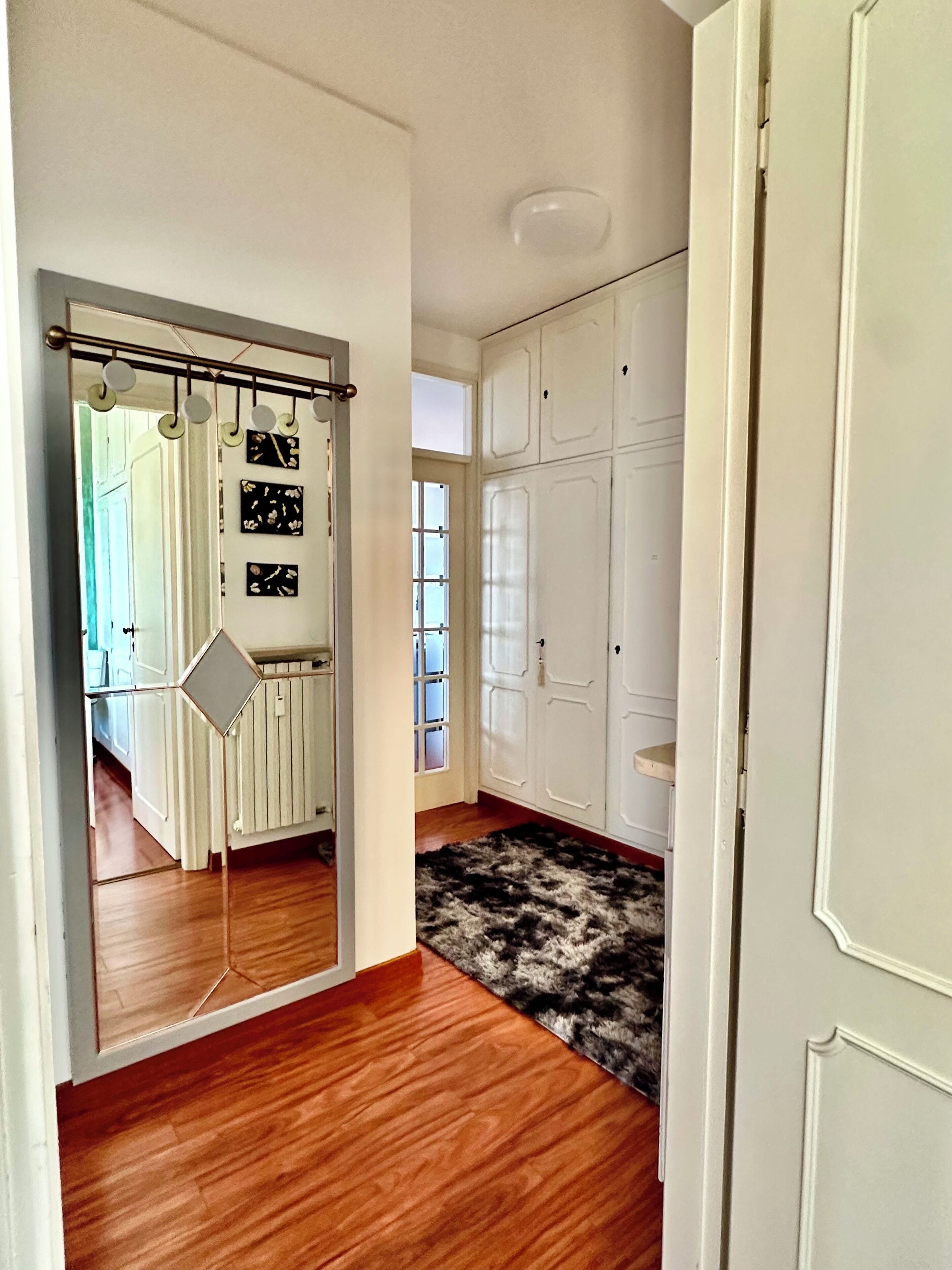 A hallway with a mirror, white cabinets, a fur rug, and a wooden floor.