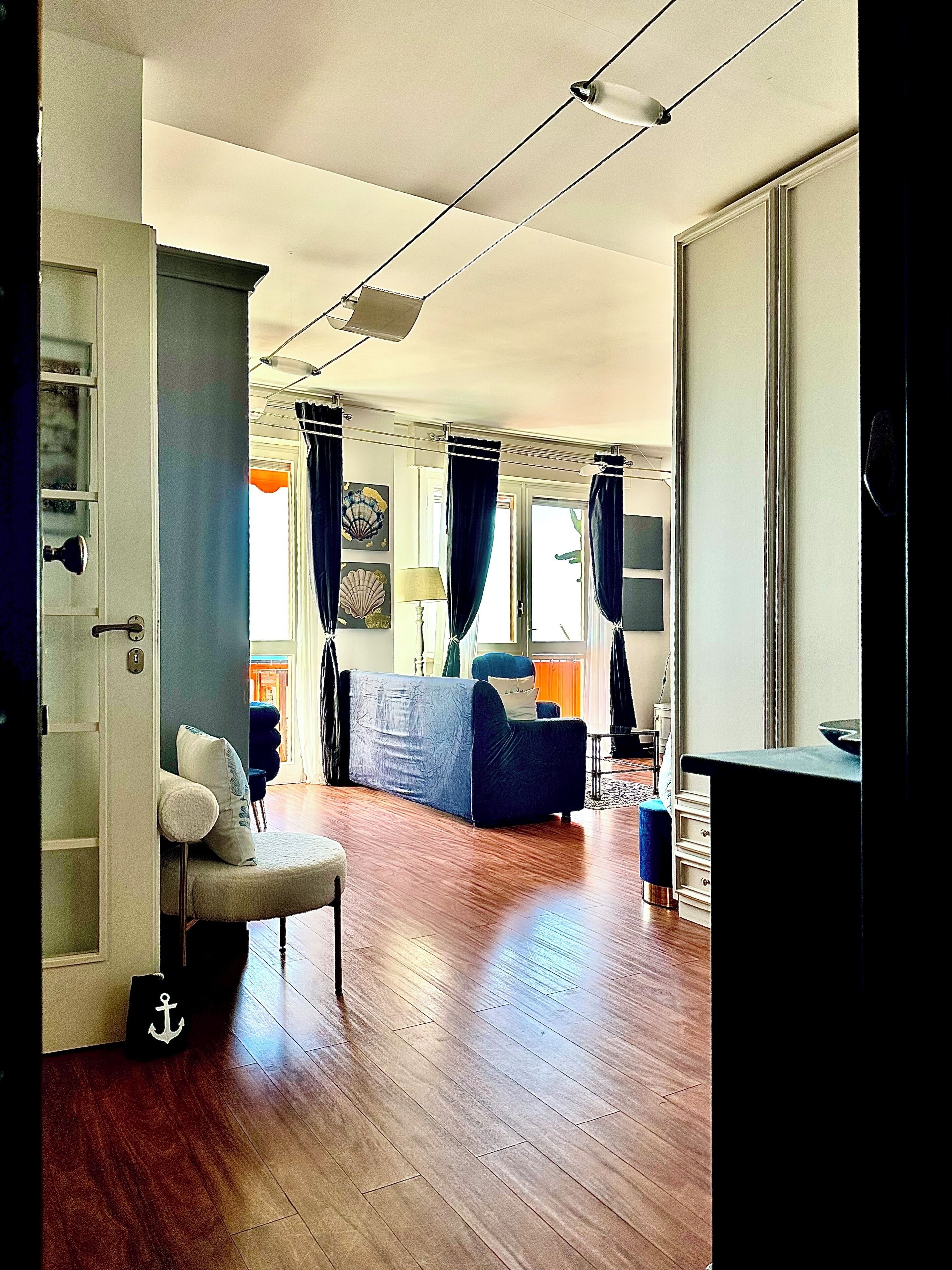 Une pièce avec un plancher en bois, un canapé bleu, une chaise, un bureau et une grande fenêtre avec des rideaux.