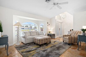 A living room with a sofa, two patterned ottomans, a patterned armchair, a lamp, a side table, and a ceiling fan. - Feel @ Home Ft Myers - 3bd - 2bh - POOL - Sleeps 8 (Fort Myers)