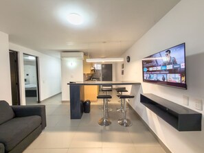 Ein moderner Wohnbereich mit Küche, einer Essecke mit Barhocker, einem an der Wand befestigten Flachbildfernseher und einer Couch.