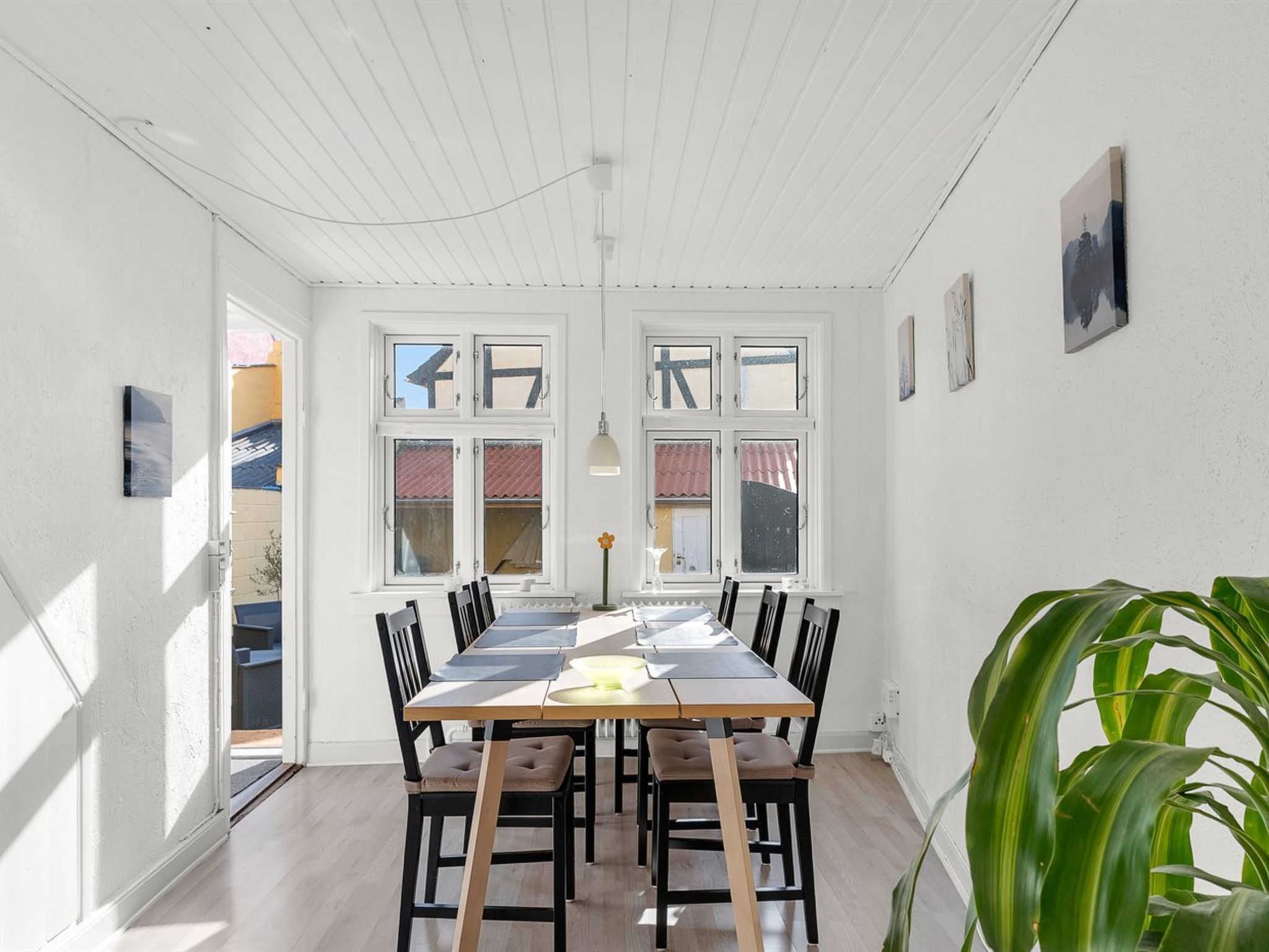 Un espace repas comprenant une longue table, plusieurs chaises, une plante et une vue dégagée grâce à de grandes fenêtres.