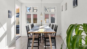 Ein Essbereich mit einem langen Tisch, mehreren Stühlen, einer Pflanze und Blick durch große Fenster.