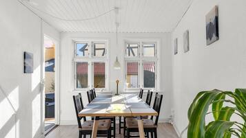 Un espace repas comprenant une longue table, plusieurs chaises, une plante et une vue dégagée grâce à de grandes fenêtres.