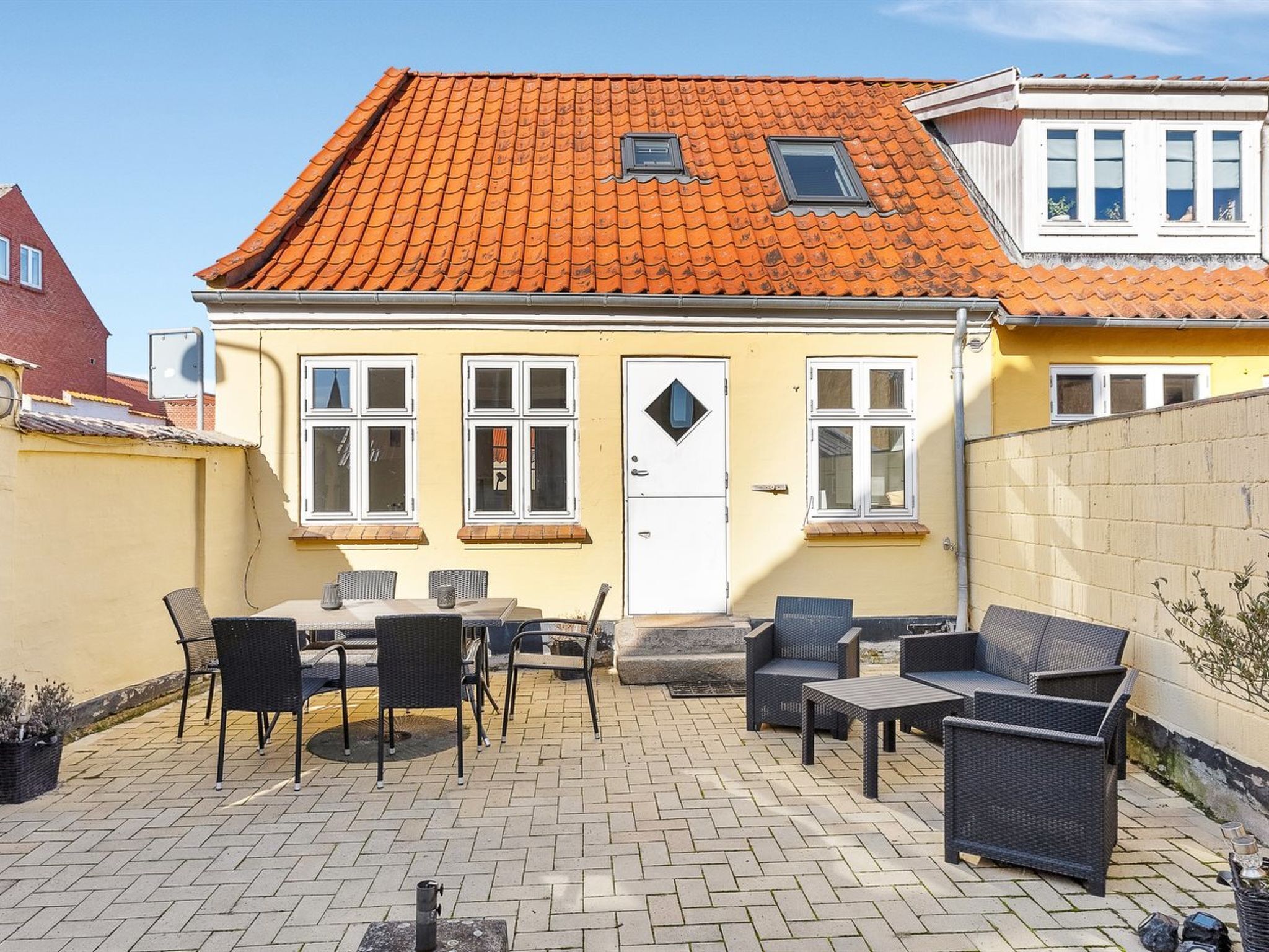 Un bâtiment jaune avec un toit recouvert de tuiles rouges, une porte blanche et une petite fenêtre.
