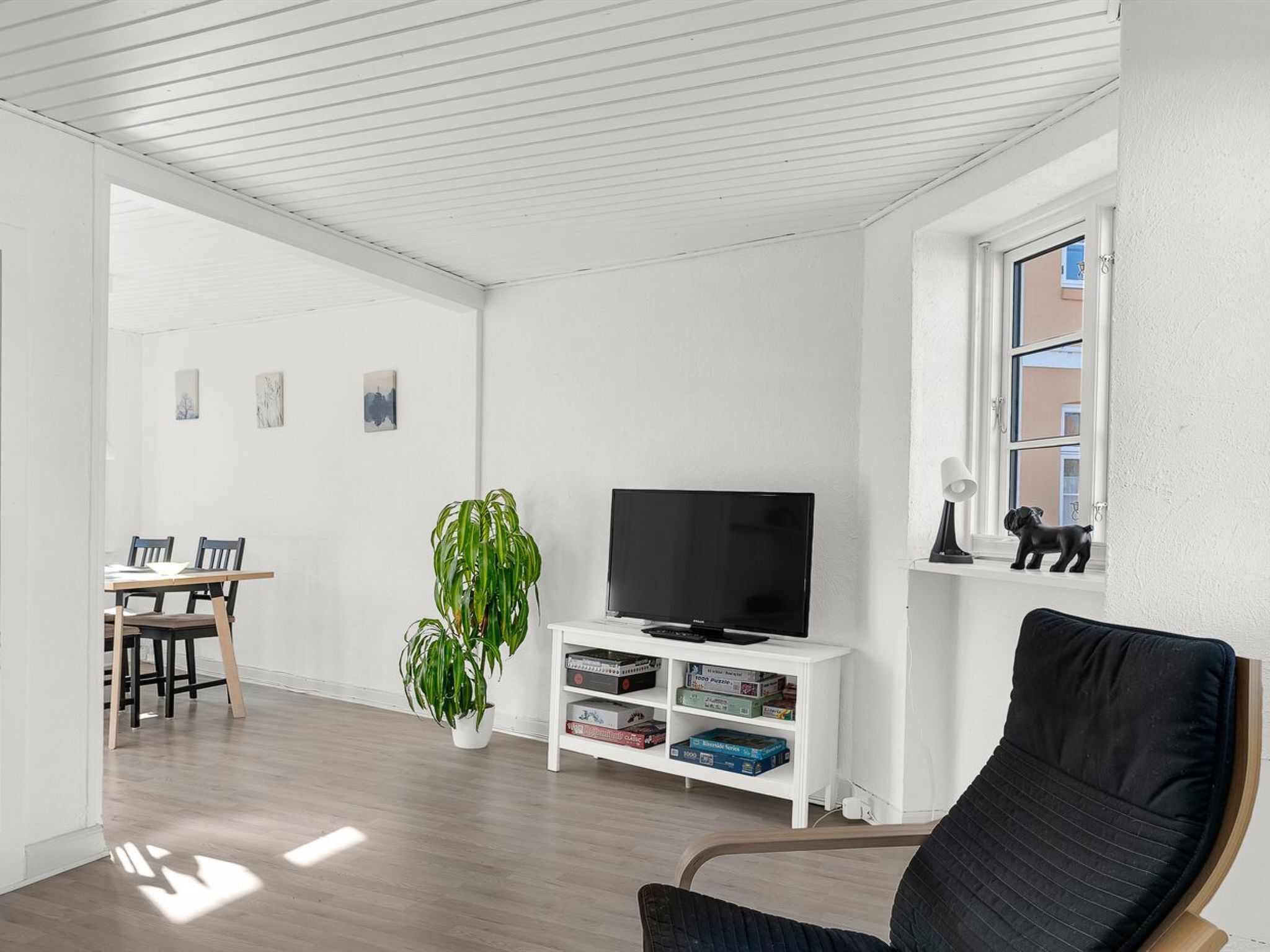 Un salon comprenant un téléviseur, une plante, une bibliothèque, une fenêtre donnant sur un beau paysage et un coin repas.