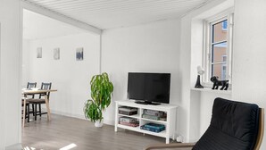 Ein Wohnzimmer mit Fernseher, Pflanze, Bücherregal, Fenster mit Aussicht und Essbereich.
