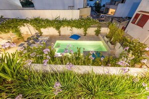Ein Poolbereich auf dem Dach mit einem rechteckigen Pool, Liegestühlen und einer Pergola mit Kletterpflanzen.