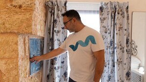 A man interacting with a wall-mounted device, possibly a thermostat, in a room with floral curtains and a white wall. - Le Terrazze Del Sud - Salve (Salve)