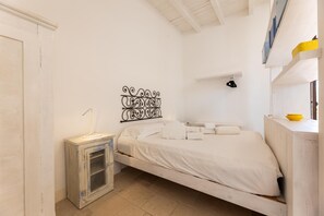 Einzimmerappartement mit einem Einzelbett, einem kleinen Nachttisch, einer wandmontierten Klimaanlage und einem dekorativen Wandkunstwerk aus Metall.