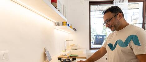 Una persona en una cocina con una encimera blanca, una estufa con cuatro fuegos y una ventana al fondo.
