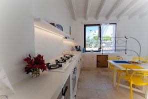 Una cucina moderna con ripiani bianchi, un'area pranzo con sedie gialle e una finestra che si affaccia sugli alberi.