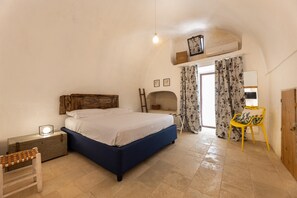 A bedroom with a bed, a wooden headboard, a nightstand, a bench, a chair, and a small table with a lamp. - Villa Terra E Sale - Salve (Salve)