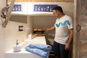 Ein Mann in einem Badezimmer mit Waschbecken, Handtuch und einer Holzkiste.