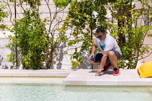 A man crouching by a pool with clear water, surrounded by greenery and a white wall. - Villa Terra E Sale - Salve (Salve)