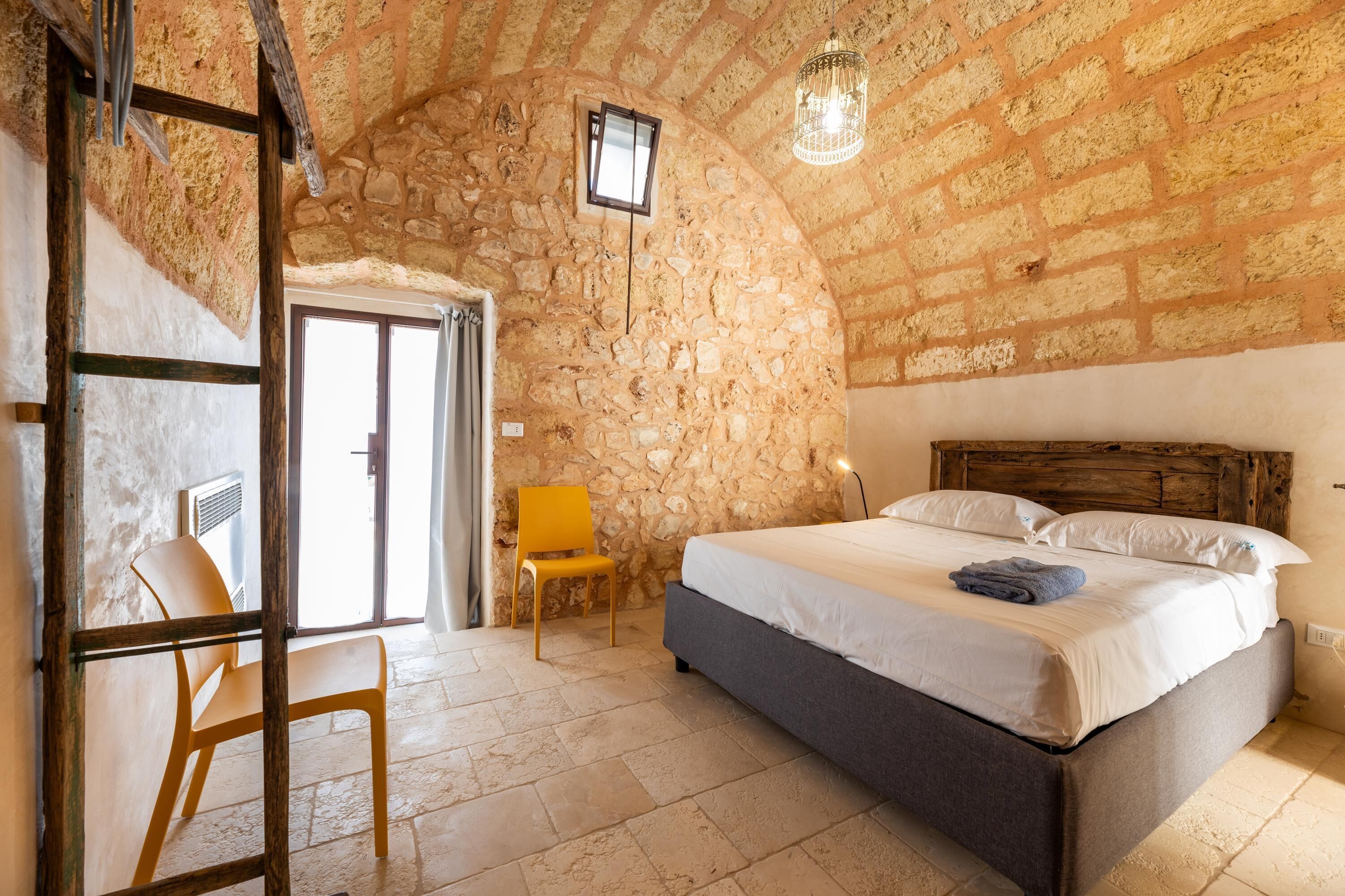 A bedroom with a stone wall, a bed, a chair, and a hanging light fixture.