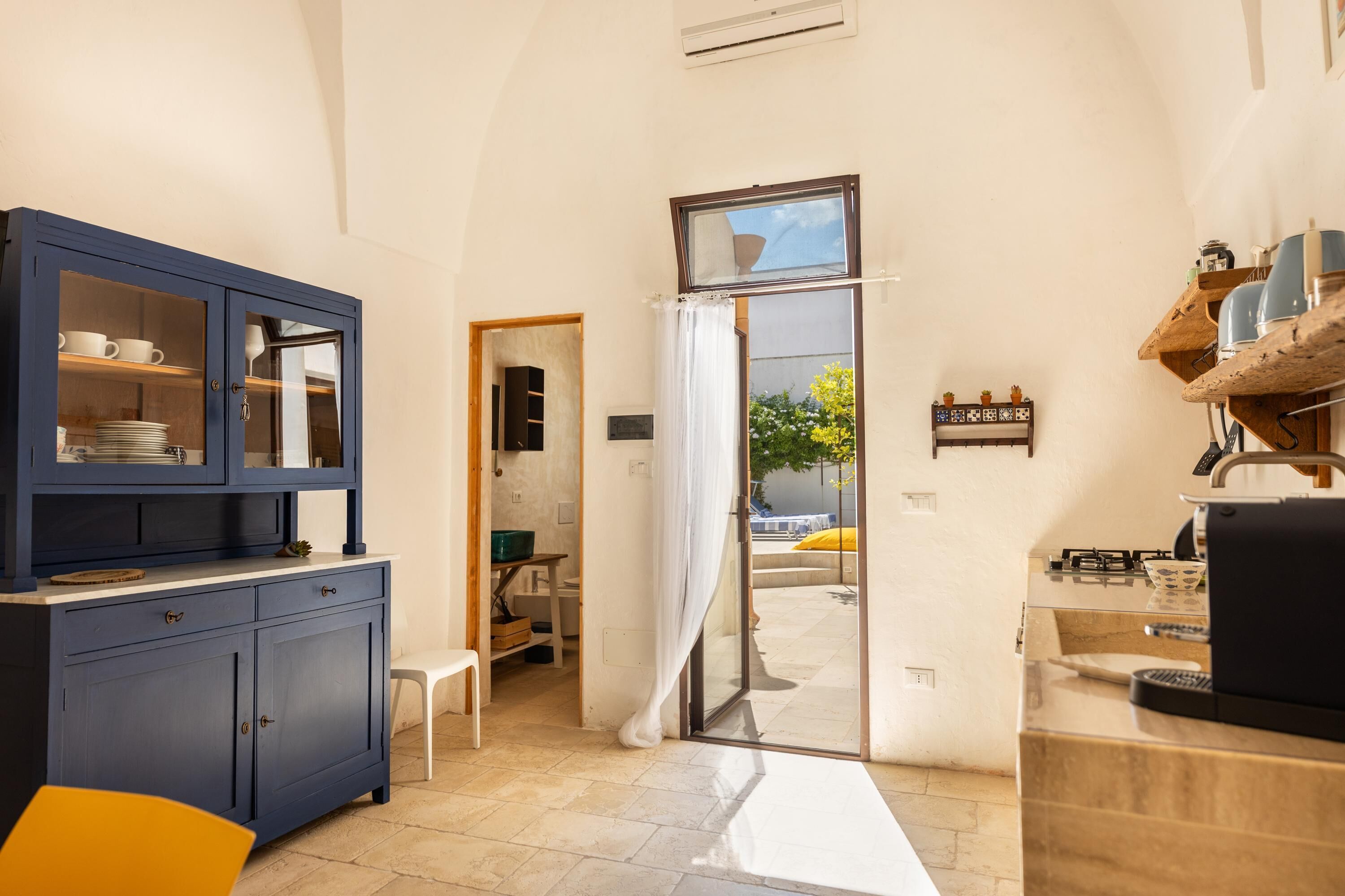 A compact kitchen with a blue cabinet, a white chair, and a view through a doorway to an outdoor area.