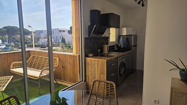 A balcony with wicker furniture, a washing machine, and a kitchen area with a microwave and oven. - Apartment with sunny terrace for 4 people 20 metres from the port  (Leucate)