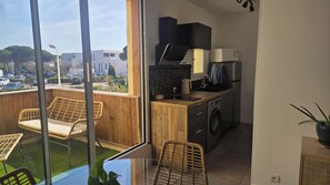 Un balcon aménagé avec des meubles en osier, un lave-linge et un coin cuisine équipé d’un four à micro-ondes et d’un four traditionnel.