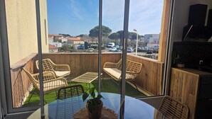 A balcony with wicker furniture, a glass table, and a view of a parking lot and buildings. - Apartment with sunny terrace for 4 people 20 metres from the port  (Leucate)