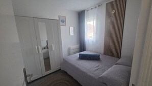 A bedroom with a bed, a wardrobe, a window with curtains, and a wall-mounted shelf. - Apartment with sunny terrace for 4 people 20 metres from the port  (Leucate)
