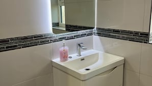 A bathroom with a white sink, a mirror, and a bottle of hand soap.