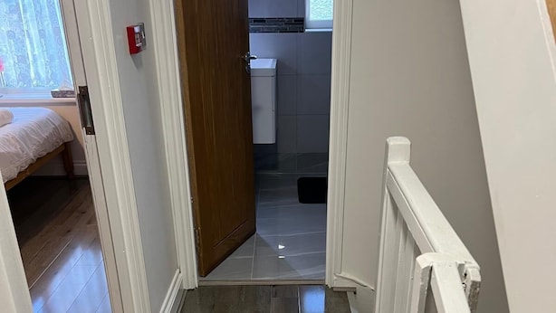 A hallway with a wooden floor leading to a bathroom with a window.